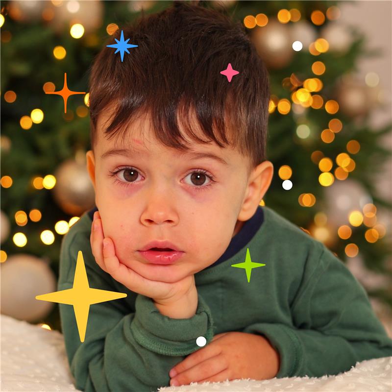 Little boy looking thoughtful resting his chin on his hand in front of a Christmas tree