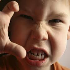 A close up of a child looking really angry with his hand out as if to grab something strongly.