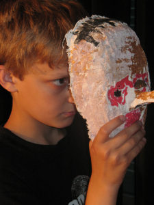 A close up of a child holding a homemade mask to his face looking serious