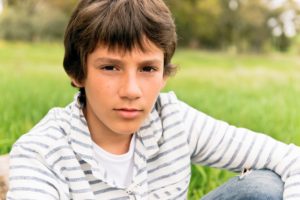 A teenage boy sat in a field on a sunny day looking straight at camera with a thoughtful look