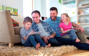 A family with 2 male adults and 1 male and 1 female child sat on the floor of a living room, playing and smiling.