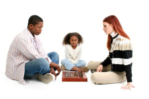 2 adults sat cross-legged facing each other with a child in the middle facing camera.